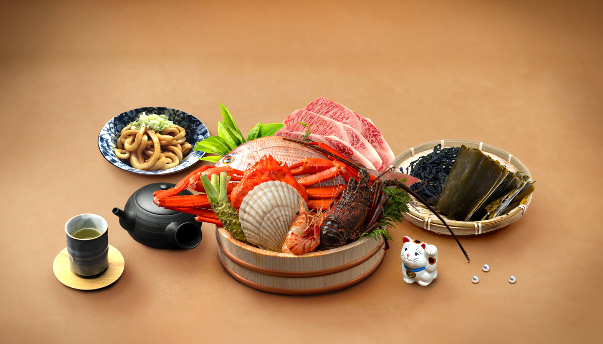 松阪牛、伊勢海老、蟹、サザエ等の食材が桶に入っている。それを取り囲むように、伊勢うどん、湯呑と急須、昆布が盛られた竹ざる、招き猫の置物、真珠が置かれている